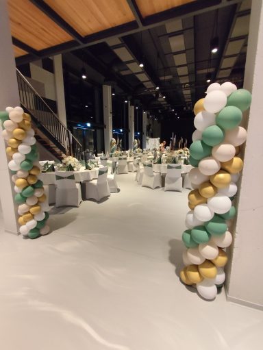 Eventdekoration und Ballondeko Waiblingen Große Eventlocation geschmückt mit weißen und gold-grünen Ballonsäulen an den Tischen.