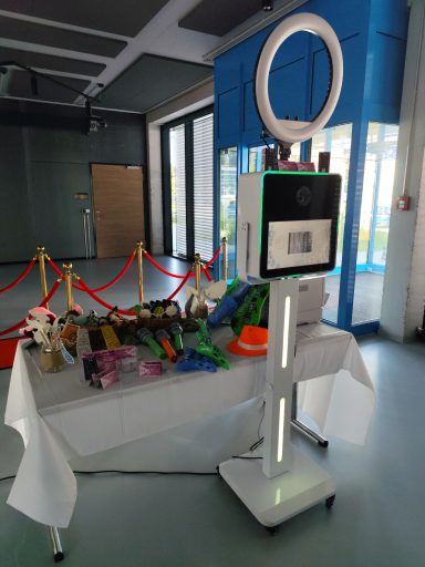 Fotobox mieten Rems-Murr-Kreis Moderne Fotobox mit Ringlicht auf Stativ neben einem Tisch voller lustiger Party-Requisiten.