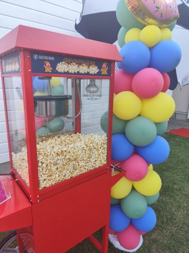 Popcornmaschine fĂĽr Events leihen Heilbronn Rote Vintage-Popcornmaschine mit Popcornwagen im Freien vor einer bunten Ballondekoration.